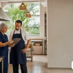 Técnico e gestor revisando checklist em cozinha de restaurante organizada.